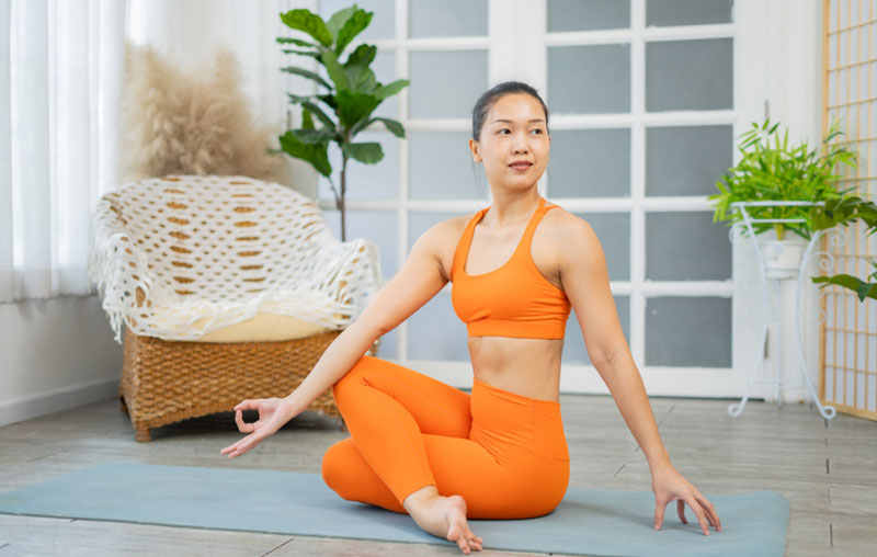 Woman in an orange sports bra and orange yoga pants in a yoga pose on the floor